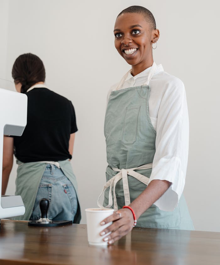 Smiling barista holding a cup of coffee behind the counter in a cafe, creating a welcoming atmosphere.